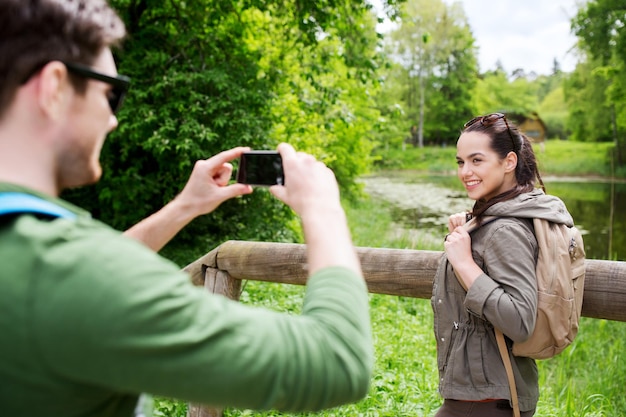concept de voyage, de randonnée, de randonnée, de tourisme et de personnes - couple souriant avec des sacs à dos prenant des photos par smartphone dans la nature