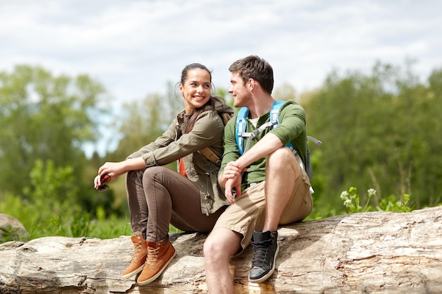 concept de voyage, de randonnée, de randonnée, de tourisme et de personnes - couple souriant avec des sacs à dos se reposant et parlant dans la nature