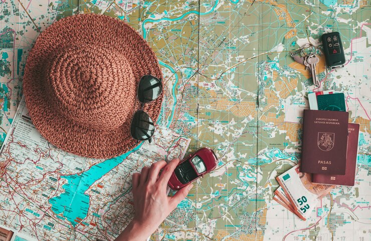Photo concept de voyage sur la route à plat. main tenant une petite voiture sur la carte à explorer. chapeau, lunettes de soleil, passeport, argent et clés sur la carte routière. planification des vacances.