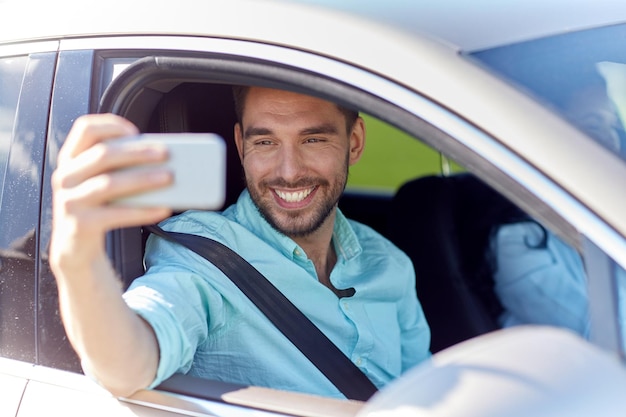 concept de voyage sur la route, de transport, de voyage, de technologie et de personnes - homme souriant heureux avec un smartphone conduisant en voiture et prenant un selfie