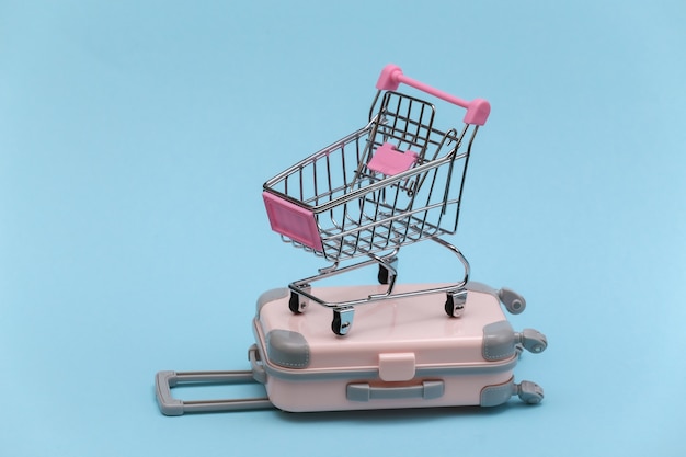 Concept de voyage et de shopping. Mini valise de voyage en plastique et chariot de supermarché sur fond bleu. Style minimaliste