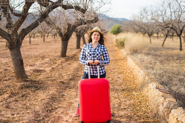 Concept de voyage, de tourisme et de personnes - heureuse jeune femme va voyager avec valise rouge et