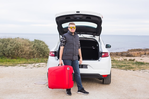 Concept de voyage, de tourisme et de personnes. homme heureux dans des verres debout avec une valise rouge