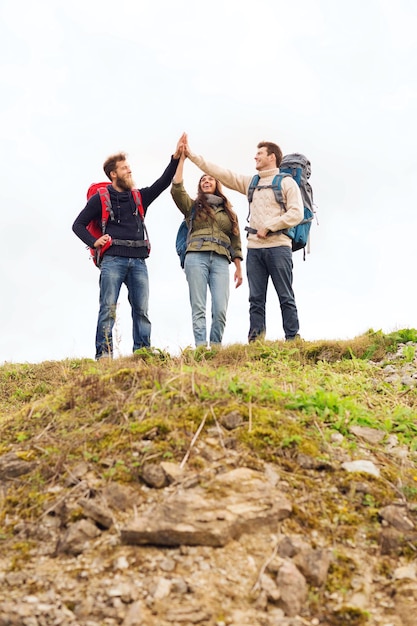 concept de voyage, de tourisme, de randonnée, de geste et de personnes - groupe d'amis souriants avec des sacs à dos faisant un high five à l'extérieur