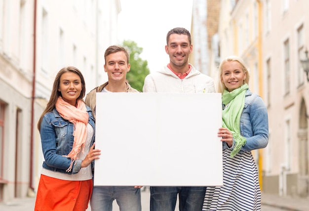 concept de voyage, de vacances et de publicité - groupe d'amis souriants avec un tableau blanc vierge dans la ville