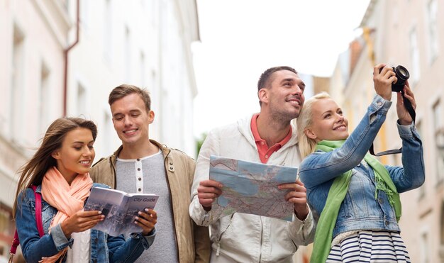 concept de voyage, de vacances, de technologie et d'amitié - groupe d'amis souriants avec guide de la ville, appareil photo et carte explorant la ville