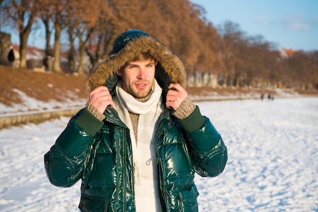 Concept de voyage et de vacances. Tenue d'hiver. Capuche de la veste de gars. Veste chaude homme fond nature enneigée. Vêtements résistants au vent. Conditions météorologiques favorables en hiver. Journée d'hiver ensoleillée. Vêtements d'hiver pour hommes.