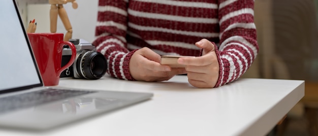 Concepteur à l'aide de smartphone sur table de travail avec ordinateur portable maquette, appareil photo et outils de peinture