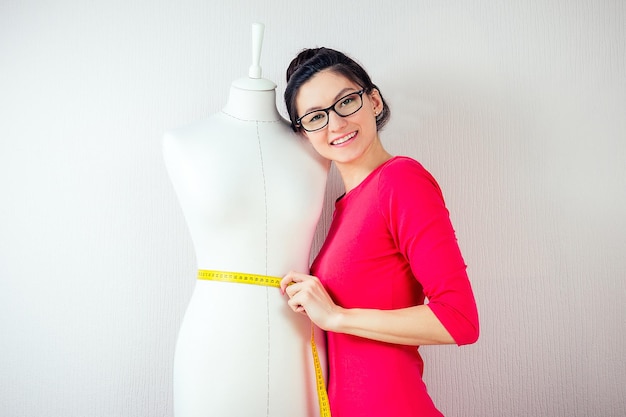 Concepteur de couturière belle fille avec des lunettes mesure la machine à coudre factice et fond blanc