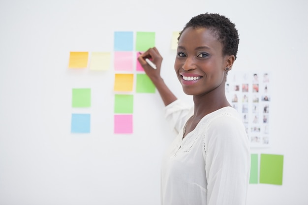 Concepteur souriant, écrivant sur des notes autocollantes et regardant la caméra