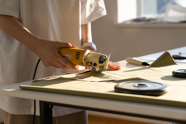 Le concepteur utilise un coupeur électrique pour couper le travail de tissu en gros plan de studio de tissu coupé sur mesure à coudre