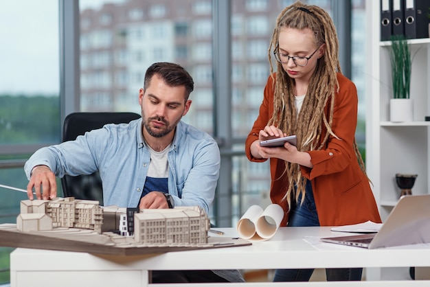 Photo des concepteurs masculins et féminins créatifs hautement qualifiés travaillant avec des maquettes de bâtiments futurs