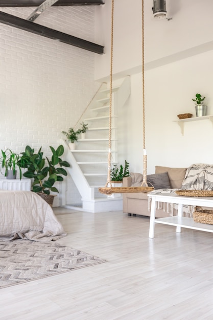 Conception de chambre de luxe dans un chalet rustique dans un style minimaliste. murs blancs, fenêtres panoramiques, éléments de décoration en bois au plafond, balançoires en corde au milieu d'une pièce spacieuse.