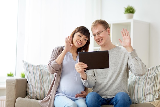 conception de la grossesse, de la technologie et des personnes - mari heureux et sa femme enceinte avec une tablette et un ordinateur en train de discuter vidéo à la maison