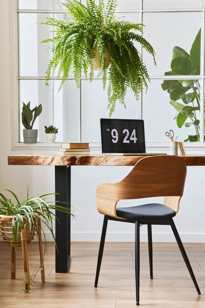 Photo conception intérieure de l'espace de bureau à domicile avec un bureau en bois élégant, une belle chaise, un ordinateur portable, des plateaux, un livre et des accessoires personnels élégants dans un décor confortable.