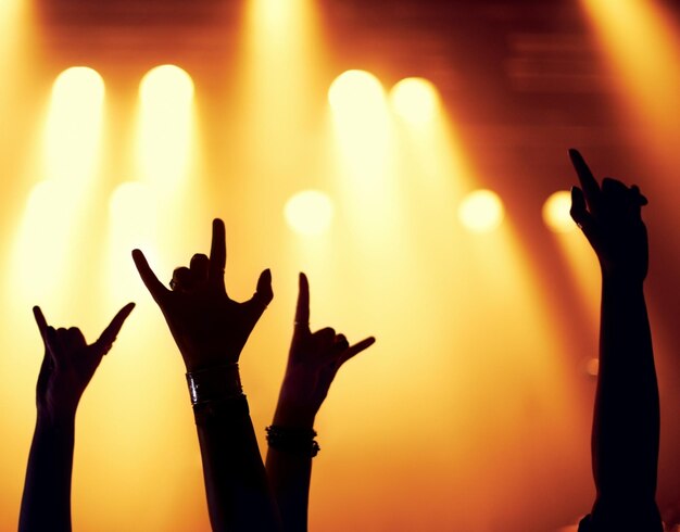 Photo concert de rock et silhouette de mains avec des fans dans la célébration d'un festival de musique et d'un événement la nuit avec de l'énergie fête de gens et emoji signe pour le métal ou soutien à la rave avec la lumière de la scène