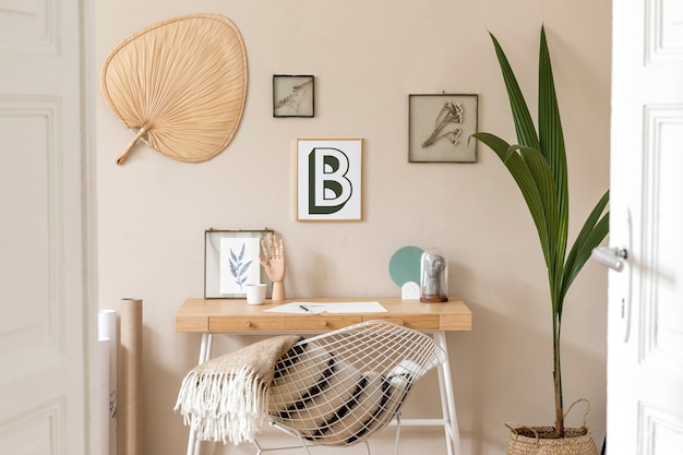 Concevez l'intérieur scandinave de l'espace de bureau à domicile avec de nombreux cadres photo, un bureau en bois, un fauteuil blanc, des plantes, un bureau et des accessoires personnels. Home staging neutre et élégant. Modèle.