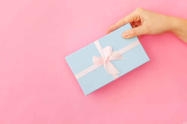 Concevez simplement une main de femme tenant une boîte-cadeau bleue isolée sur fond tendance coloré pastel rose. Célébration de la Saint-Valentin d'anniversaire de Noël Nouvel An présente le concept romantique. Espace de copie