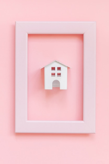 Concevez simplement avec une maison de jouet blanche miniature dans un cadre rose isolé sur fond tendance coloré pastel rose