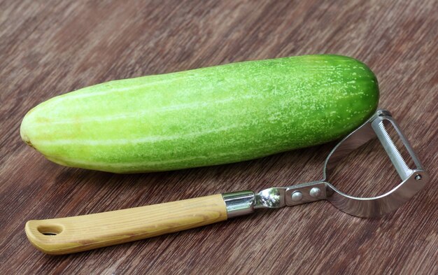 Concombre frais avec éplucheur sur une surface en bois