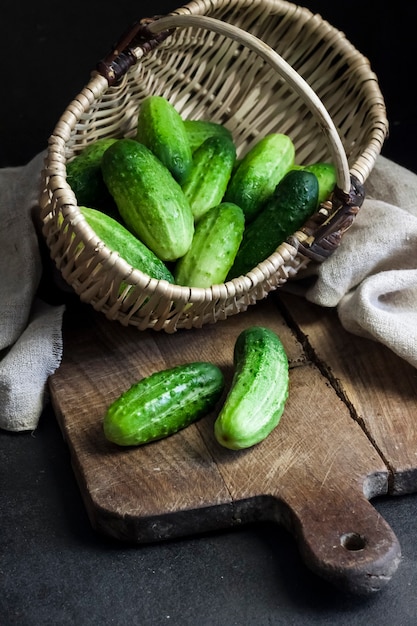 Concombres frais dans un panier en osier sur planche de bois sur fond noir.