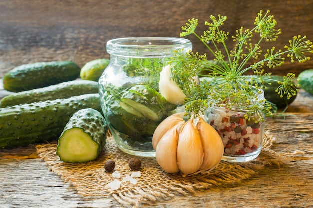 Concombres marinés, ail et épices à mariner dans un bocal sur une table en bois.