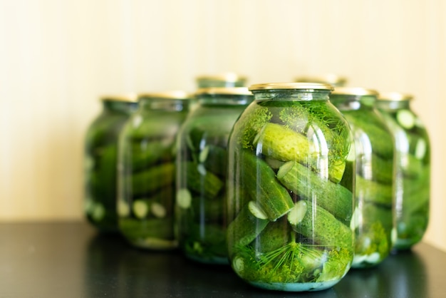 Concombres marinés dans un bocal en verre sur une table en bois grise.