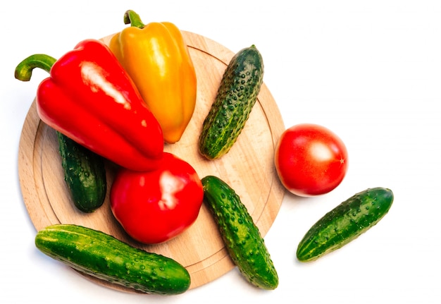 concombres, poivrons et tomates sur une planche à découper en bois blanc