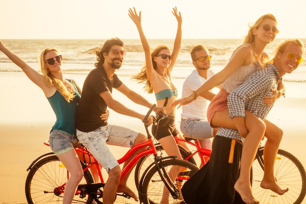 Concours d'amis heureux sur le cycle et l'homme sportif donnant à leur petite amie des promenades sur le dos des vacances de liberté d'été sur la mer