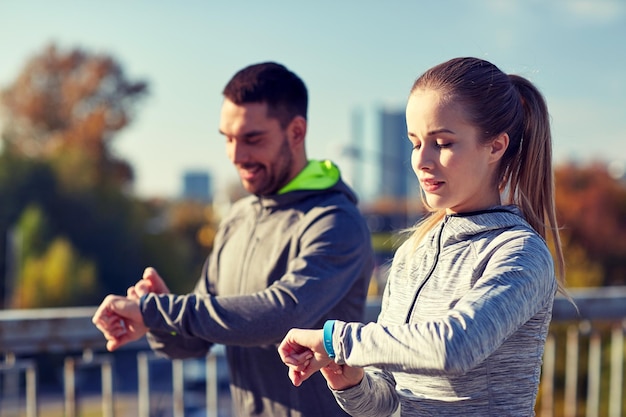 condition physique, sport, personnes, technologie et concept de mode de vie sain - couple souriant avec montre de fréquence cardiaque courant sur le pont de l'autoroute de la ville