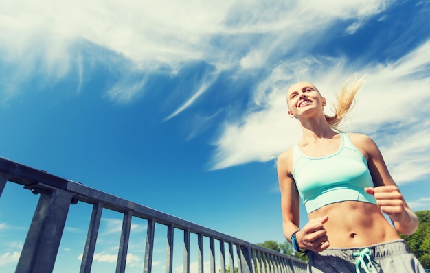 condition physique, sport, personnes, technologie et concept de mode de vie sain - jeune femme souriante avec montre de fréquence cardiaque courant à l'extérieur