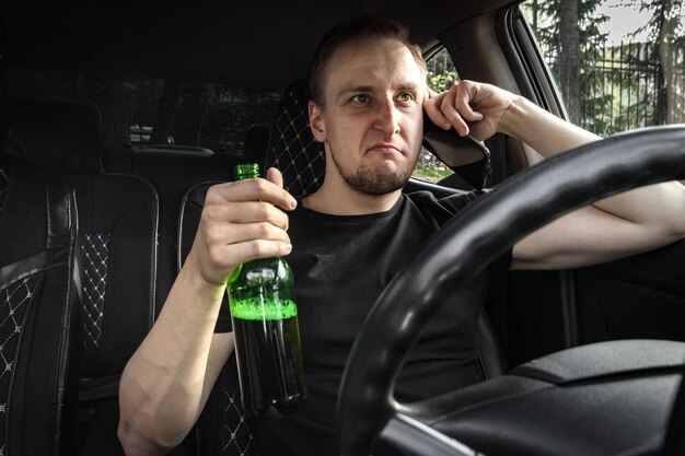 Conducteur agressif en état d'ivresse avec une bouteille d'alcool conduisant une voiture parler au téléphone concept de conduite en état d'alcool