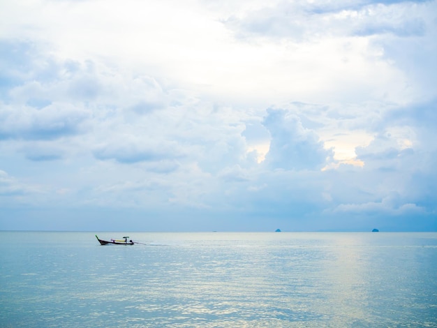 Conducteur de bateau sur un bateau traditionnel à longue queue dans la mer avec fond nuageux et ciel au coucher du soleil dans un style minimaliste thaïlandais