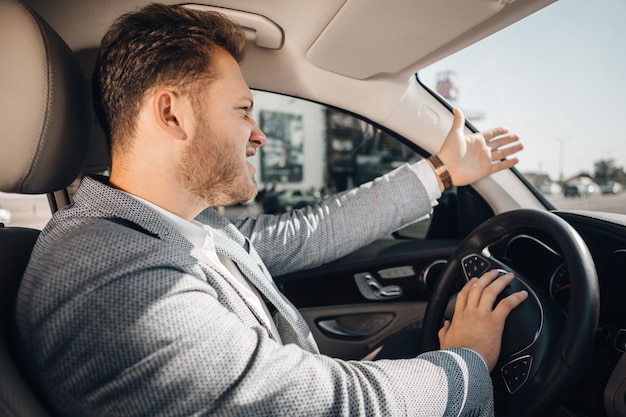 Conducteur en colère dans un embouteillage perdant son autoprotection et faisant signe de laisser sa voiture partir. Être en retard.