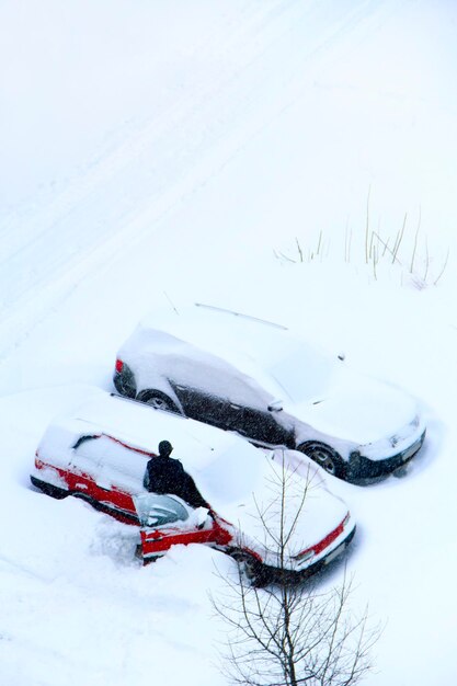 Un conducteur essayant de libérer sa voiture de la captivité neigeuse Des voitures garées couvertes de neige mauvais temps en ville Jour neigeux Scène urbaine Concept météorologique Automobiles piégées dans la neige