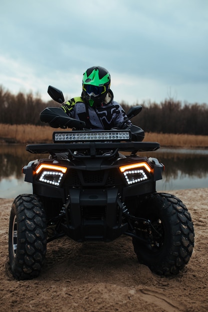 Le conducteur est assis sur un quad en arrière-plan la rivière et le sable. concept sport et extrême