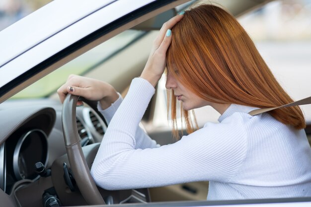 Conducteur de femme yound fatigué triste assis derrière le volant de la voiture dans les embouteillages.