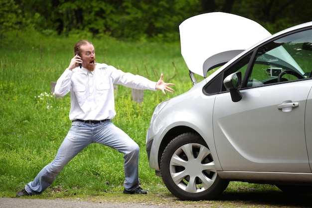 Conducteur furieux avec le téléphone portable d'une voiture cassée au bord de la route