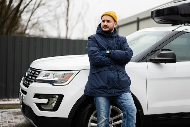 Le conducteur de l'homme porte une veste et un chapeau jaune contre sa voiture SUV américaine avec galerie de toit par temps froid