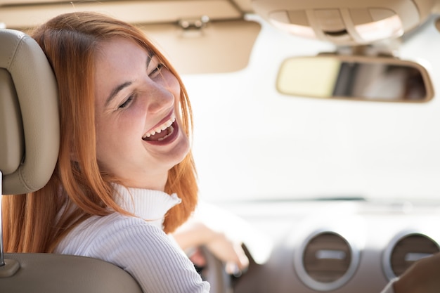 Conducteur de jeune femme rousse au volant d'une voiture souriant joyeusement.