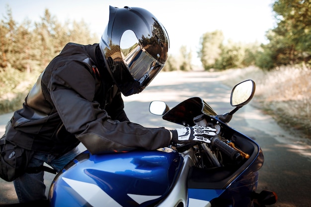 Le conducteur de moto en casque et veste en cuir est assis sur une moto de sport sur la route sur fond de forêt. Beau fond, une place pour l'espace de copie