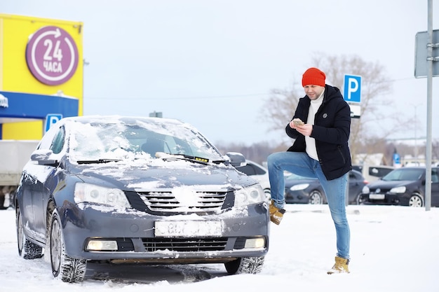 Un conducteur se tient devant une voiture. Le propriétaire nettoie la voiture de la neige en hiver. Voiture après une chute de neige.