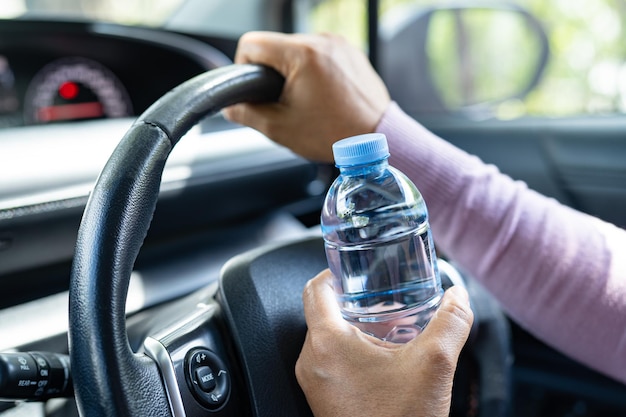 Une conductrice asiatique tenant une bouteille pour boire de l'eau en conduisant une voiture Une bouteille d'eau chaude en plastique provoque un incendie