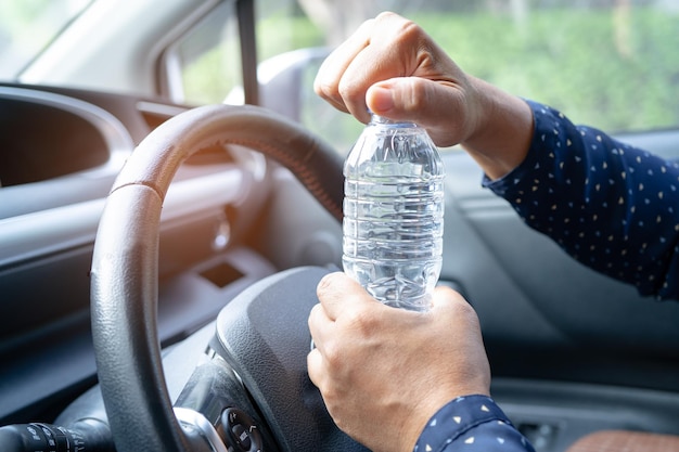 Une conductrice asiatique tenant une bouteille pour boire de l'eau en conduisant une voiture Une bouteille d'eau chaude en plastique provoque un incendie