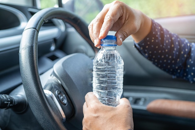 Une conductrice asiatique tenant une bouteille pour boire de l'eau en conduisant une voiture Une bouteille d'eau chaude en plastique provoque un incendie