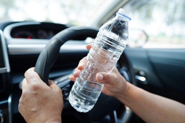 Une conductrice asiatique tient de l'eau froide pour boire dans une voiture dangereuse et risque un accident