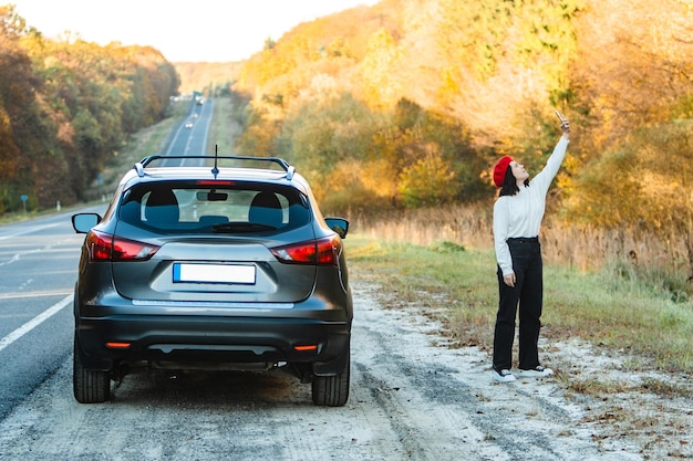 Une conductrice essaie d'attraper le réseau au téléphone près de la voiture debout sur le bord de la route