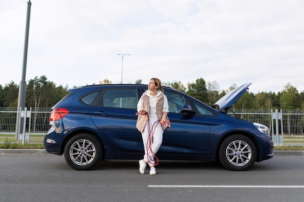 Conductrice fatiguée tenant un voltmètre de voiture sur le fond d'une voiture cassée