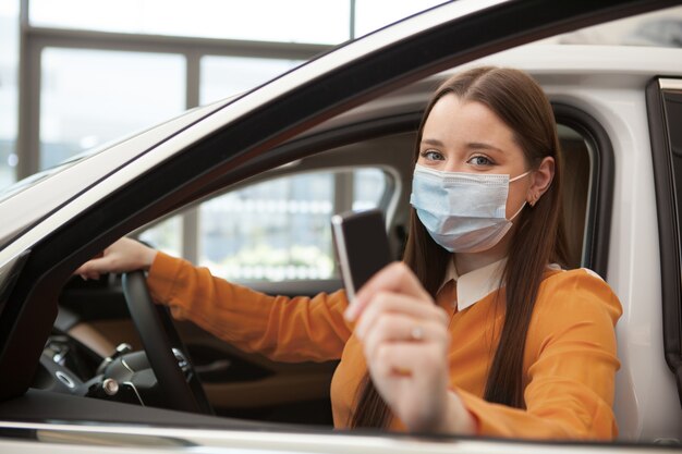 Conductrice portant un masque médical, tenant la clé de la voiture devant la caméra