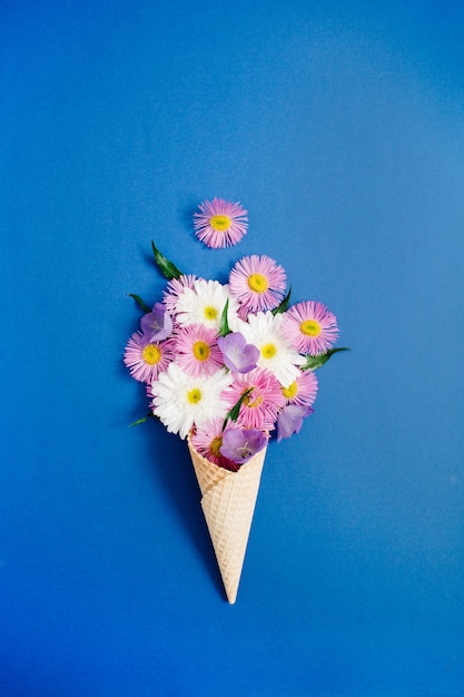 Cône de gaufre avec bouquet de fleurs de camomille sur fond bleu. Mise à plat, vue de dessus